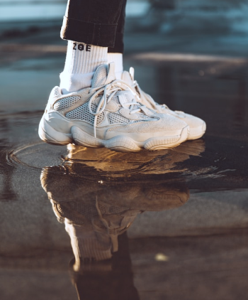 Tênis branco com meias brancas em um chão molhado.