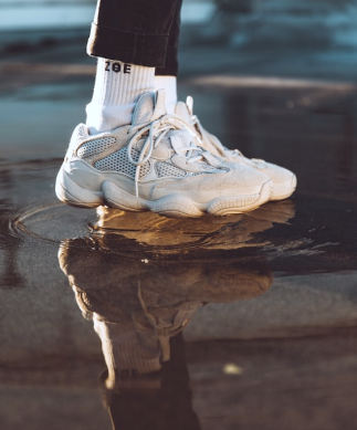 Tênis branco com meias brancas em um chão molhado.