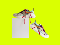 Tênis branco com detalhes azul, verde, marrom e vermelho apoiado em uma caixa branca.