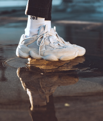 Tênis branco com meias brancas em um chão molhado.